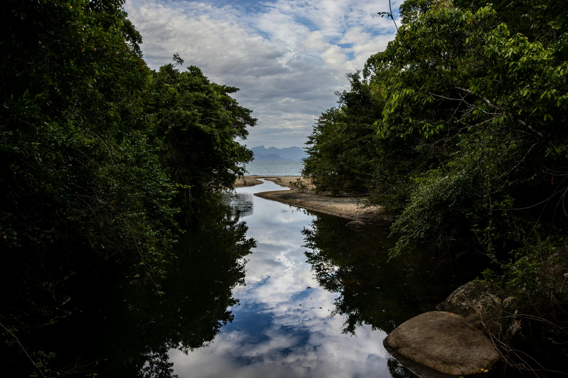 Picturesque river and lush greenery in Angra dos Reis, Brazil, reflecting a cloudy sky.
