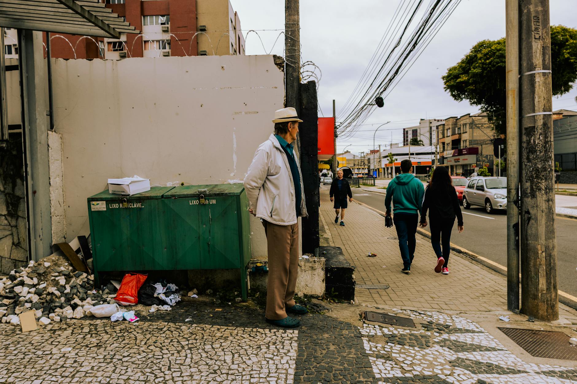 People walking along a sidewalk in Curitiba, Brazil, depicting an urban setting with street traffic.