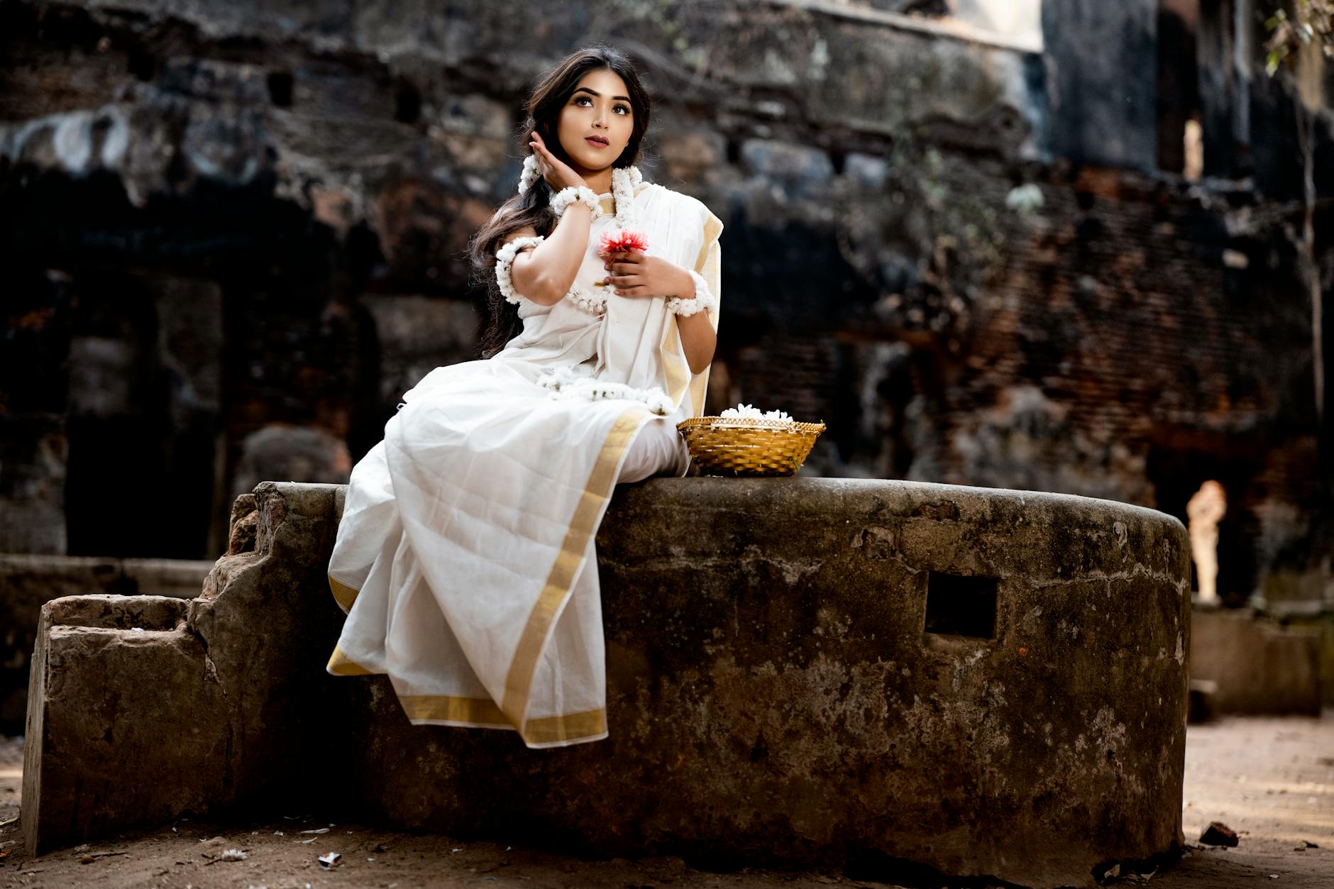 A young Indian woman in a traditional white saree poses outdoors, showcasing elegance and culture.