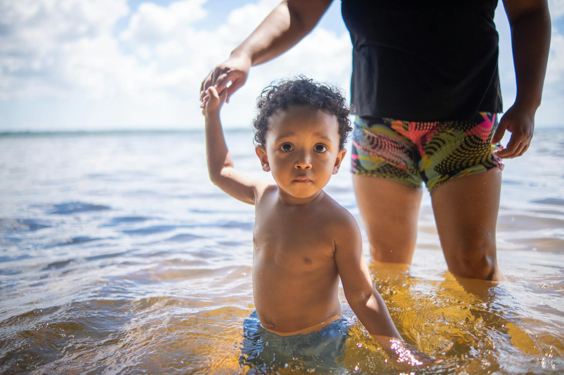 A happy child playing in the water at a sunny beach with a guardian.