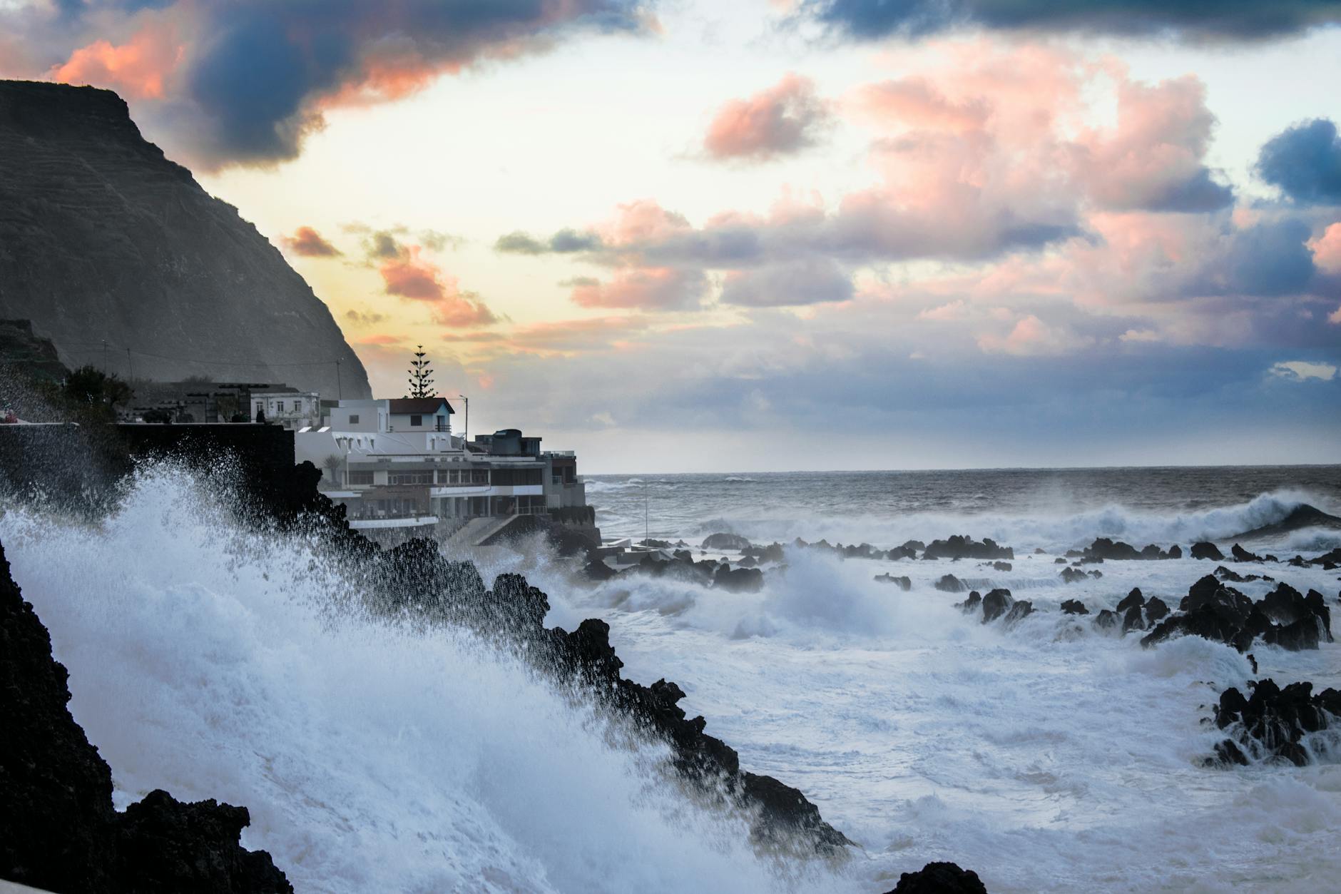 Dramatic coastal scene with waves crashing against rocks during a vivid sunset, showcasing nature's power.