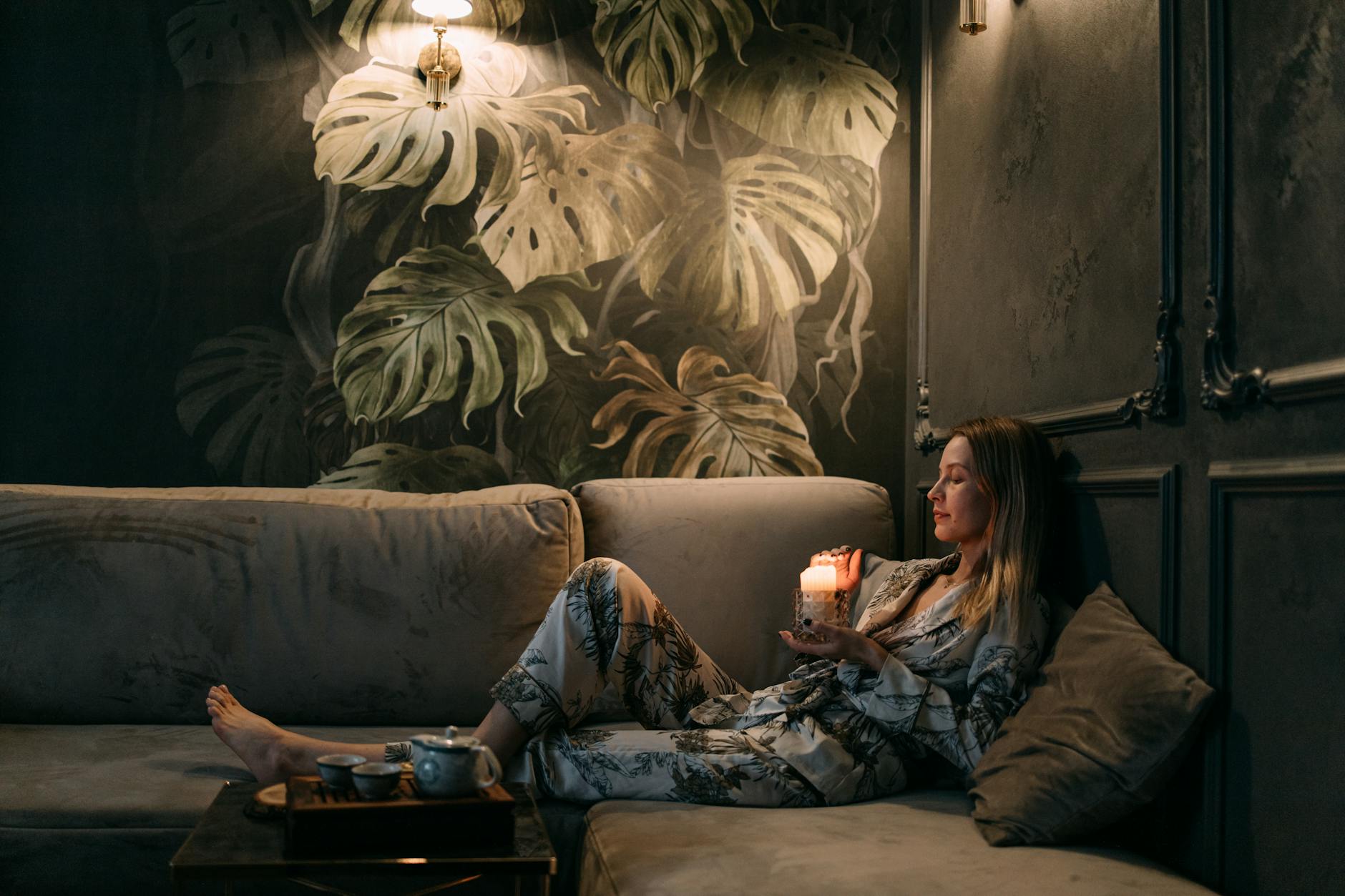 A woman relaxes on a sofa with a candle, creating a calming atmosphere indoors.