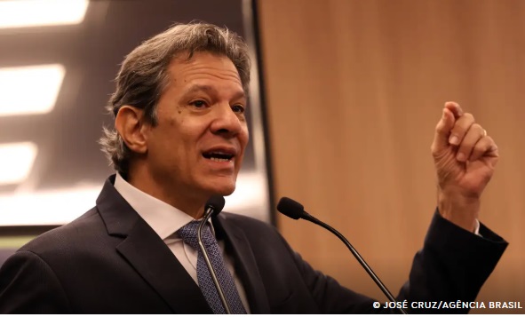 Ministro da Fazenda Fernando Haddad em coletiva de imprensa, ao fundo um logo da Receita Federal.
