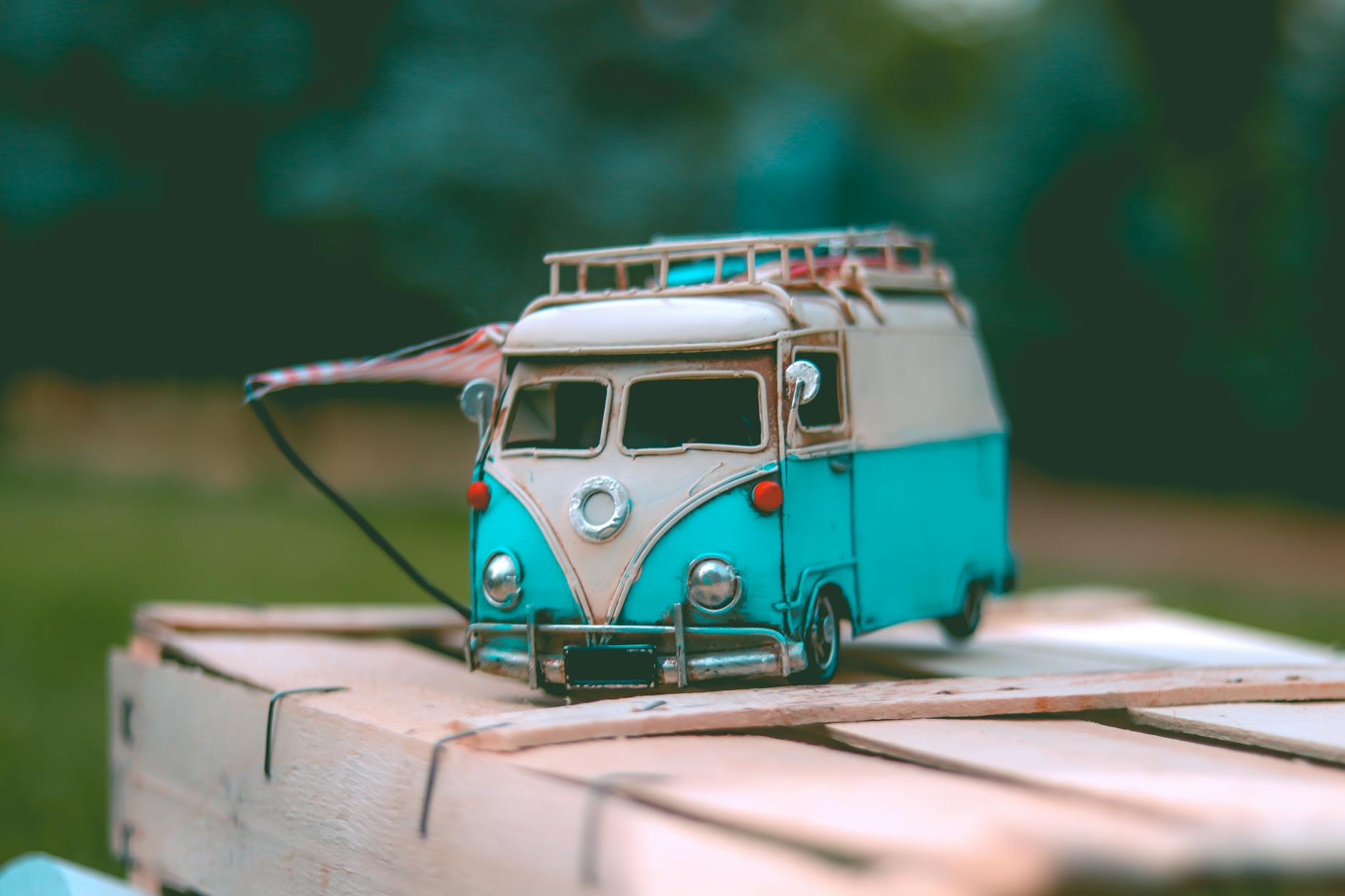 Close-up of a vintage miniature blue van toy placed on a wooden surface outdoors, capturing a nostalgic scene.