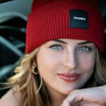 Close-up portrait of a woman wearing a red beanie inside a car, exuding confidence and style.