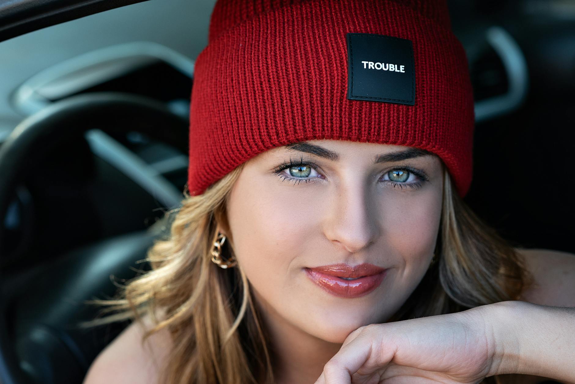 Close-up portrait of a woman wearing a red beanie inside a car, exuding confidence and style.
