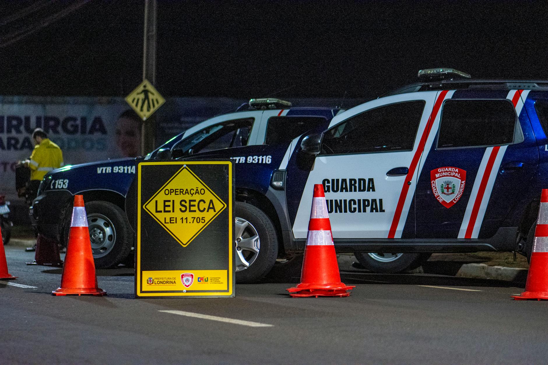 Night scene of a traffic checkpoint by the Municipal Guard in Londrina, Brasil, featuring police vehicles and cones.