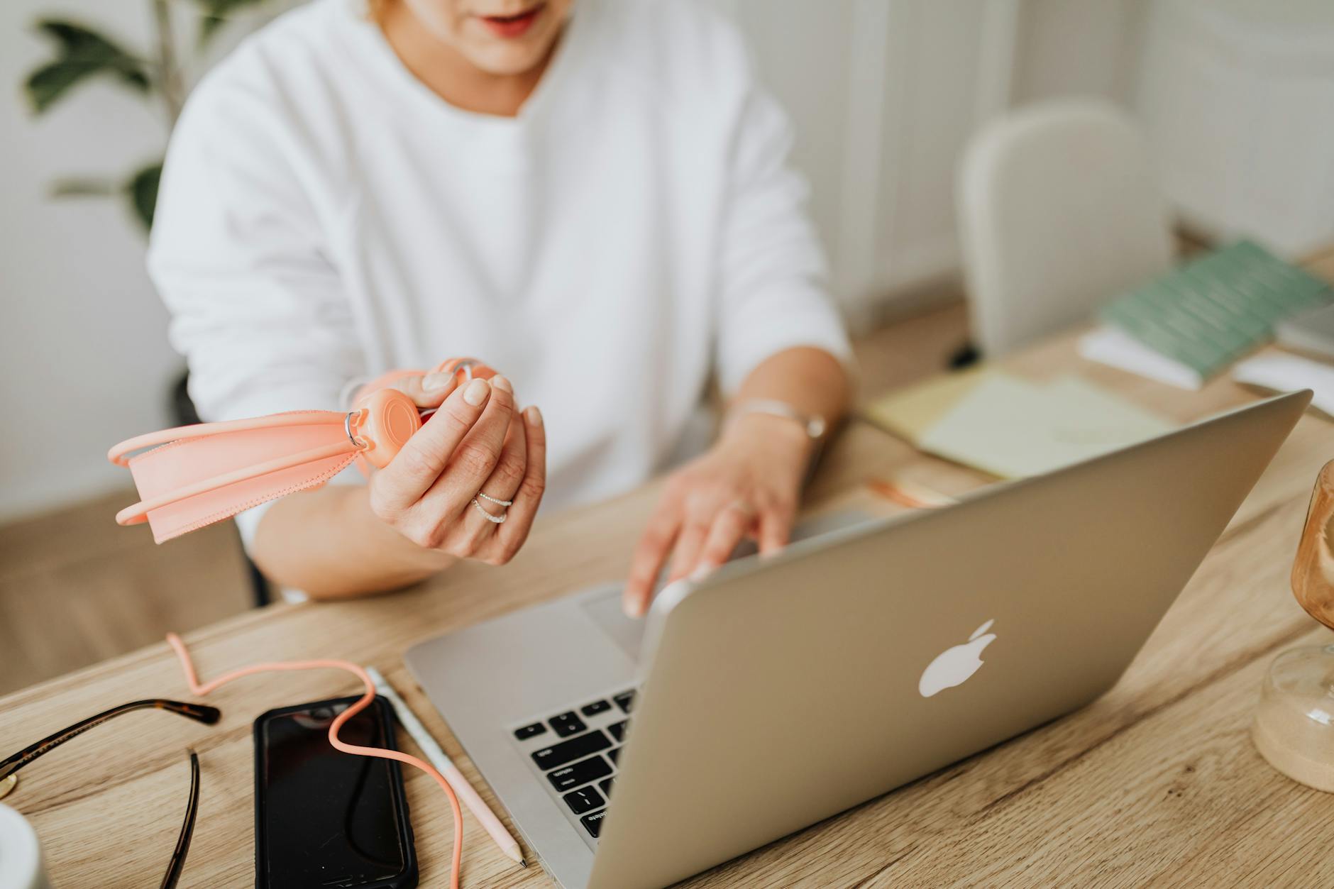 Woman using a laptop at a wooden desk with various accessories and a smartphone.