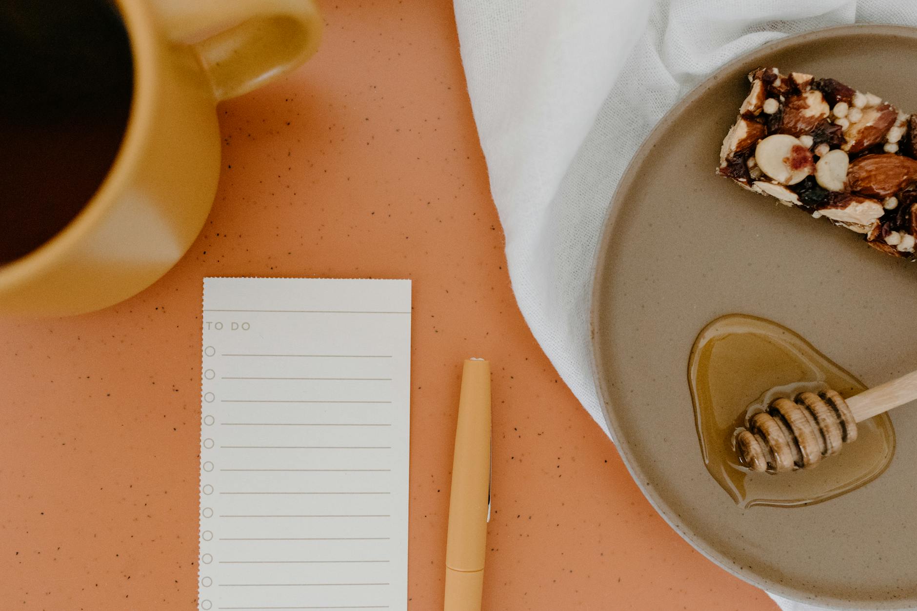 A cozy flat lay featuring a cup of coffee, nuts with honey, and a to-do list on an orange table.