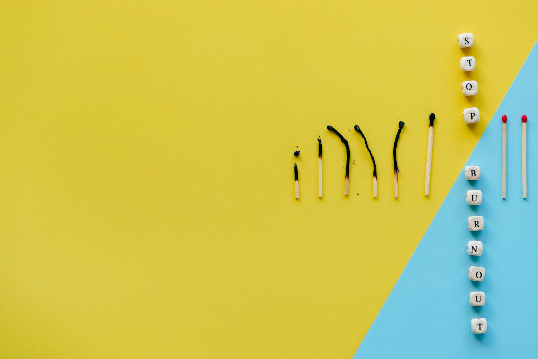 Artistic representation of burnout using matches and blocks spelling 'STOP BURNOUT' on colorful background.