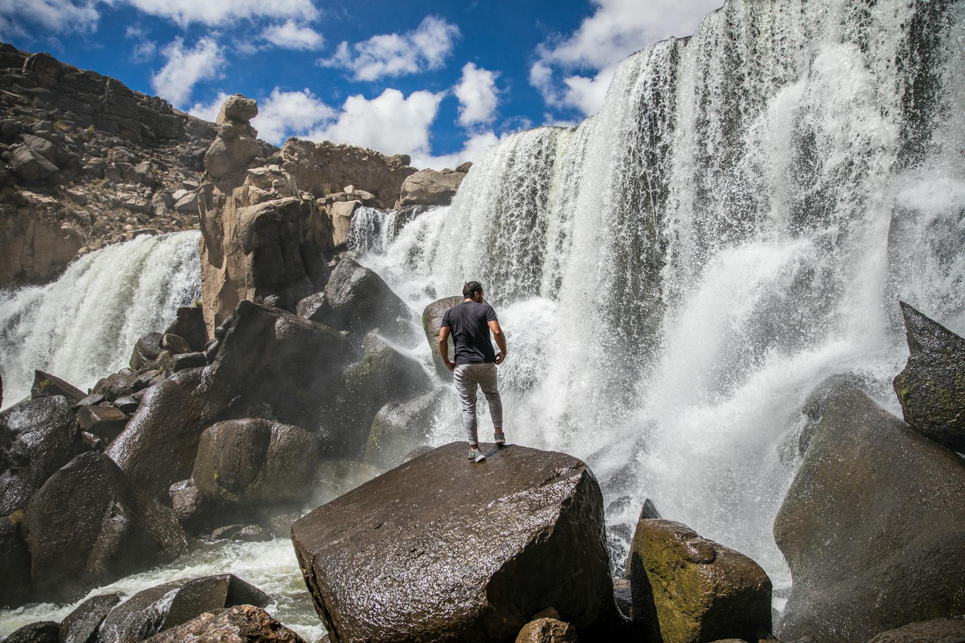 Person on boulders facing a waterfall under a bright blue sky in Novo Progresso, Brazil.