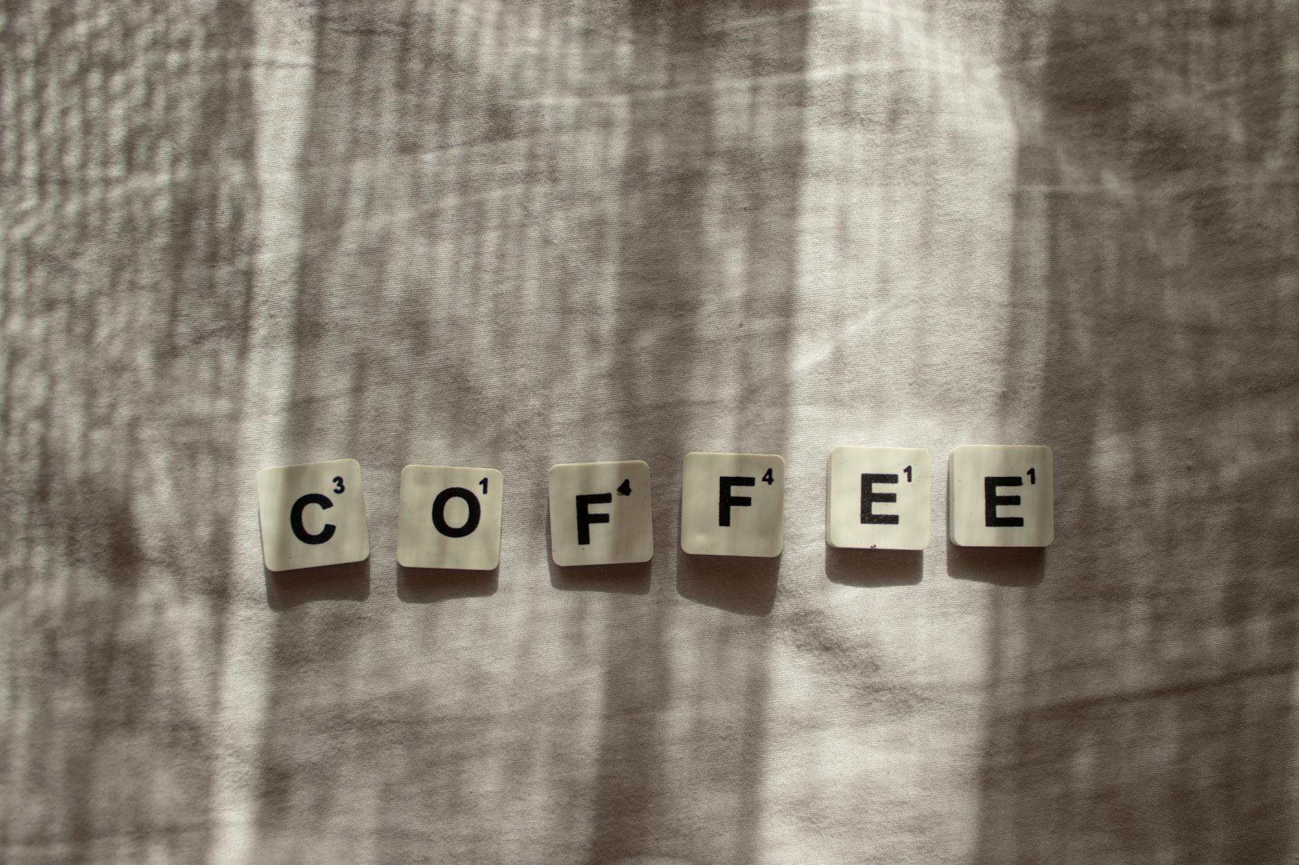 Scrabble tiles spelling 'coffee' with light and shadow on fabric surface. Perfect for coffee and word lovers.